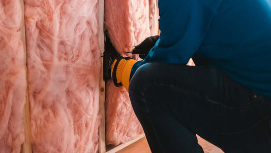 Worker installing pink fiberglass insulation inside a wall for shed improvement, part of 6 ways to insulate your metal garage.